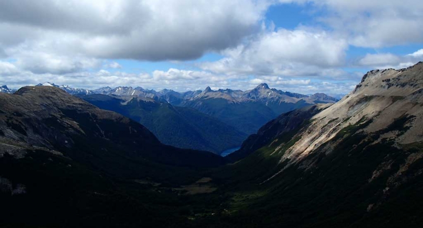 A vast mountainous landscape appears blue in the distance under a blue sky dotted with white clouds. 